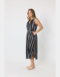 A woman modeling a sleeveless midi dress with vertical black and white stripes, a matching tie belt, and a side slit, standing against a plain light gray studio background.