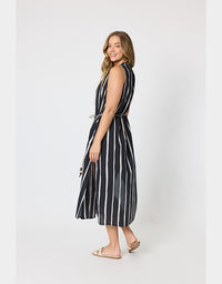 A woman modeling a sleeveless midi dress with vertical black and white stripes, standing in profile against a light gray studio background.