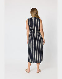 A woman viewed from the back wearing a sleeveless midi dress with vertical white stripes on a black base, standing against a plain light gray studio background.
