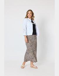 A woman modeling a light blue eyelet button-up shirt over a black top and a leopard-print midi skirt, paired with beige slide sandals, against a plain light gray studio background.