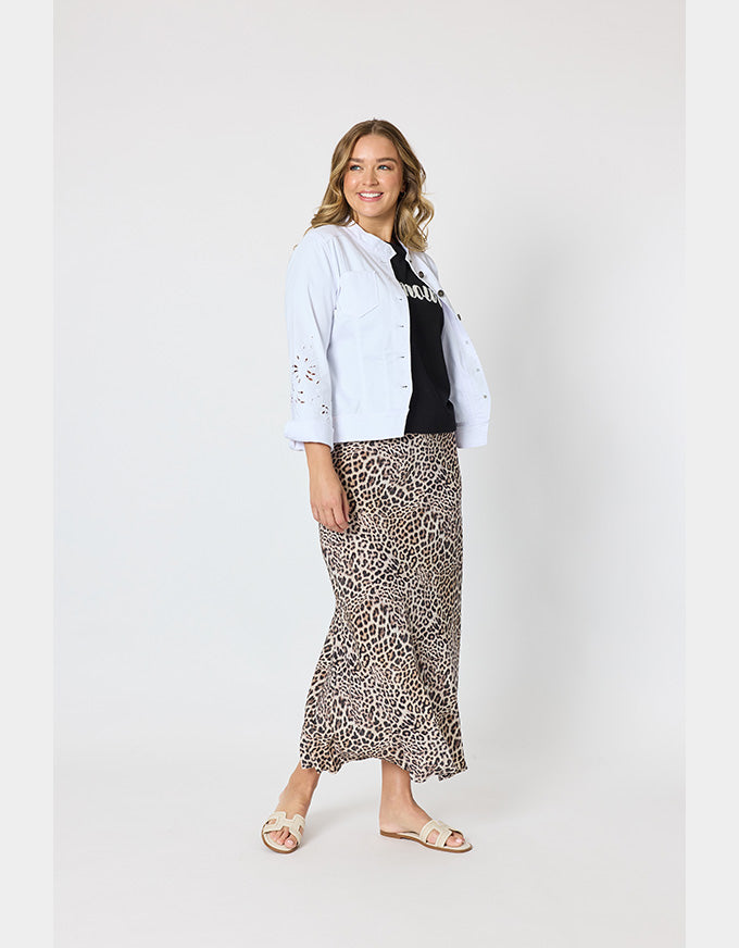 A woman modeling a light blue eyelet button-up shirt over a black top and a leopard-print midi skirt, paired with beige slide sandals, against a plain light gray studio background.