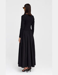 A woman wearing a long black dress with a fitted long-sleeve bodice and a full, flowing skirt, shown from the back against a plain light gray studio background.