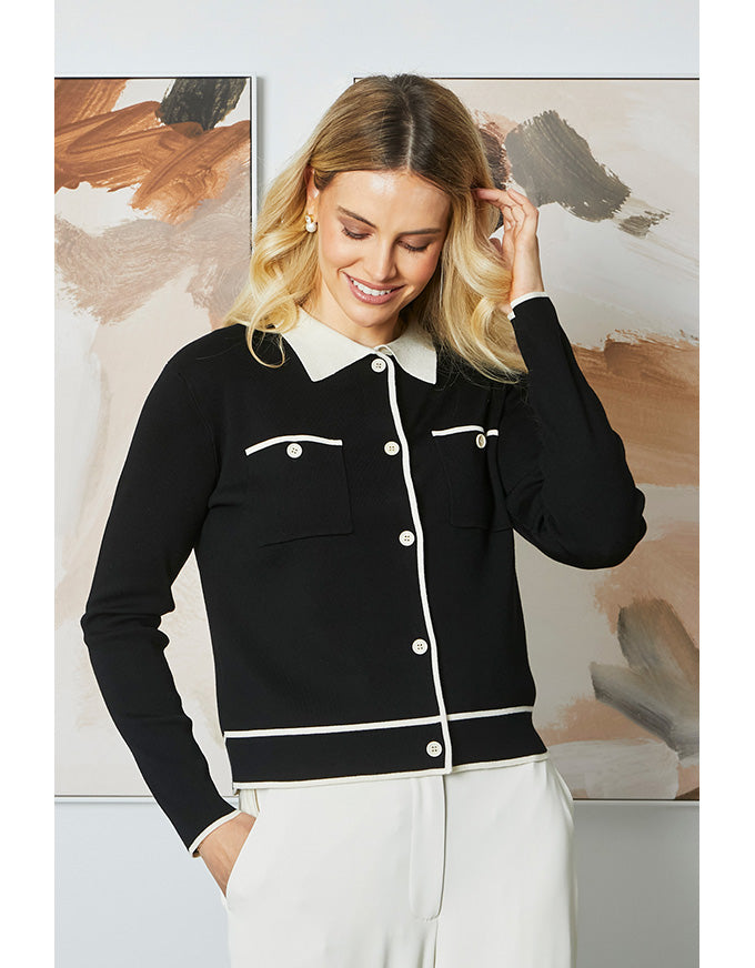 Woman wearing a black jacket with white collar and buttons in front of abstract art.