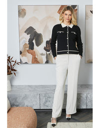 Woman wearing a black jacket with white buttons and white pants in a room with abstract art on the wall.