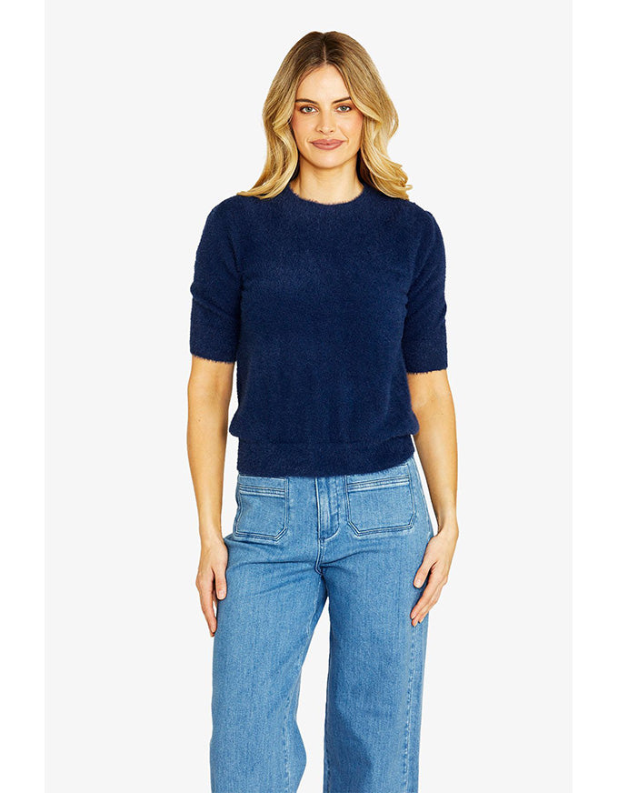 Woman wearing a navy sweater and blue jeans on a white background