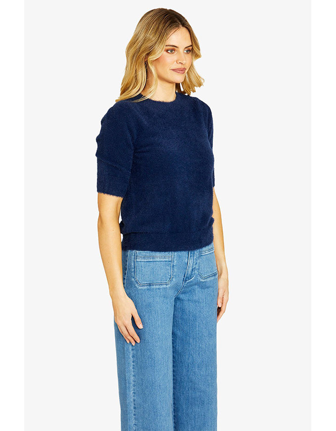 Woman wearing a navy sweater and blue jeans on a white background