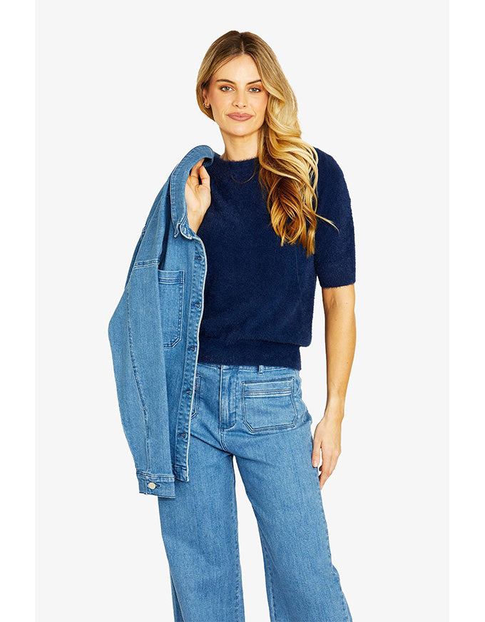 Woman wearing a navy sweater and blue jeans with a denim jacket on a white background