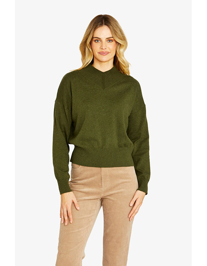 Woman wearing a green sweater and beige pants on a white background