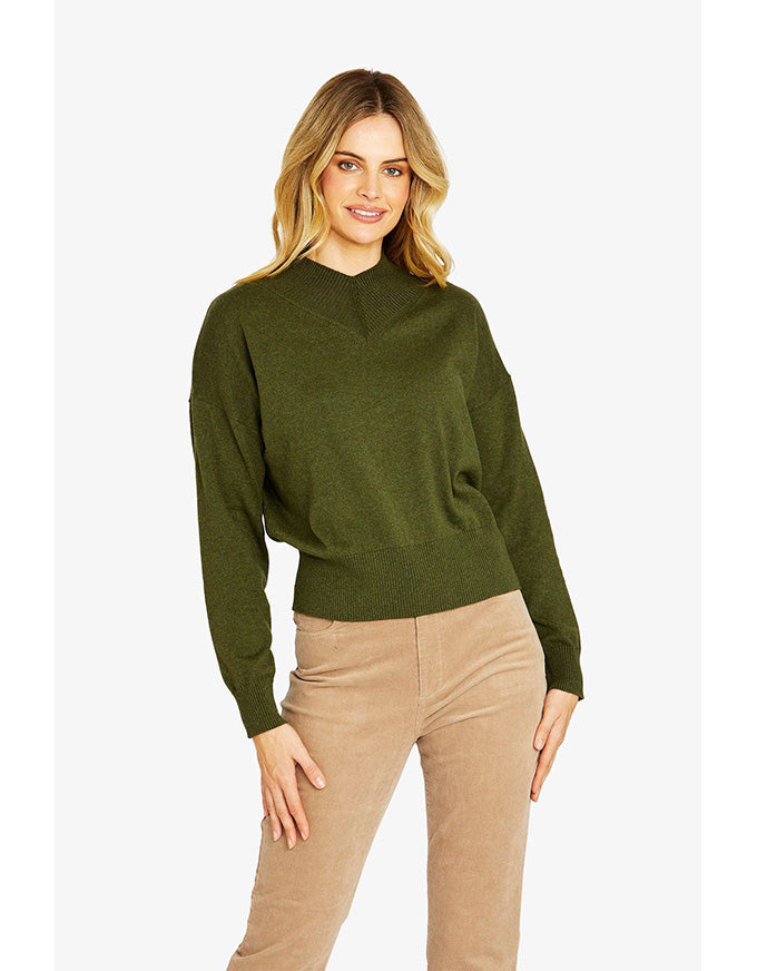 Woman wearing a green sweater and beige pants on a white background