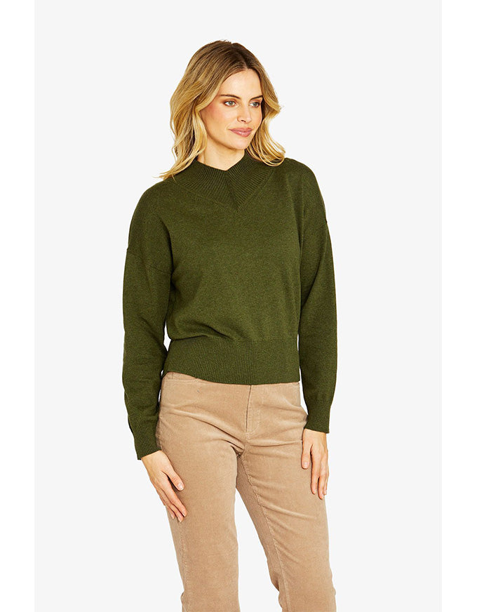 Woman wearing a green sweater and beige pants on a white background