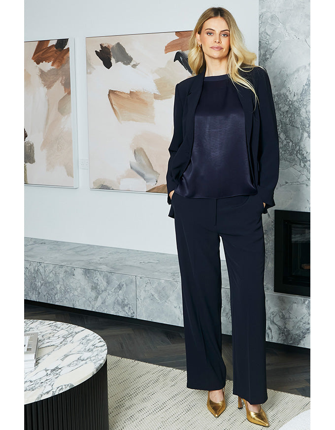 Woman in a navy suit standing in a modern interior setting with abstract art on the wall.