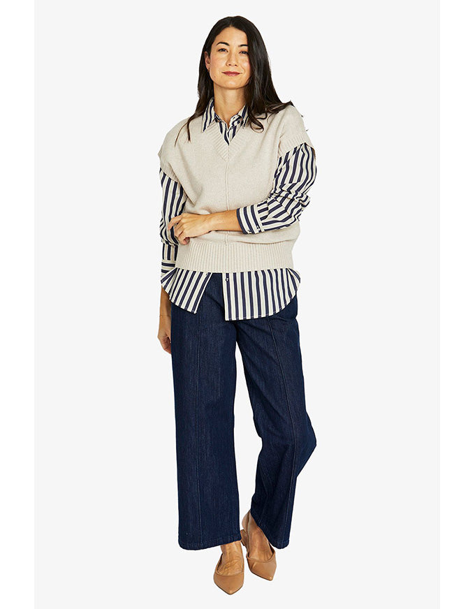 Woman wearing a striped shirt, vest, and navy pants on a white background