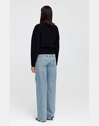 A model shown from the back wearing a black long-sleeve knit top and light-wash wide-leg denim jeans against a plain light gray studio background.