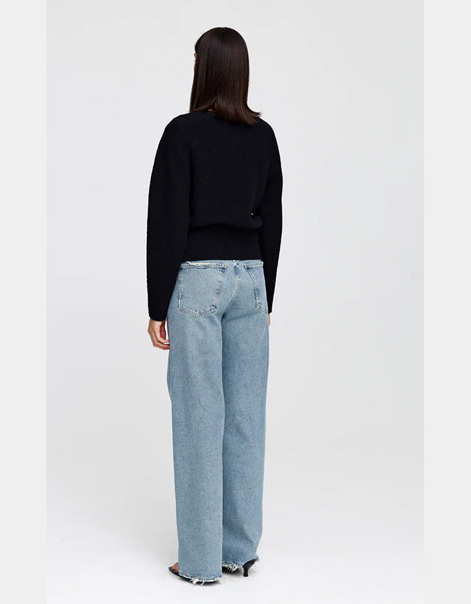 A model shown from the back wearing a black long-sleeve knit top and light-wash wide-leg denim jeans against a plain light gray studio background.