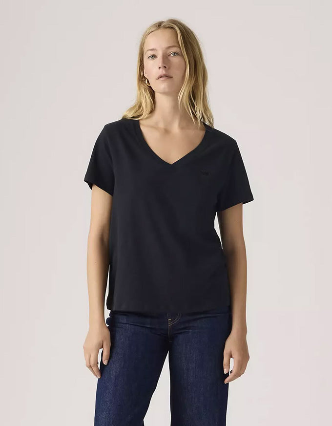 Woman wearing a black V-neck t-shirt and blue jeans against a plain background
