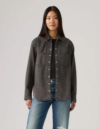 Person wearing a dark denim jacket and blue jeans on a light gray background