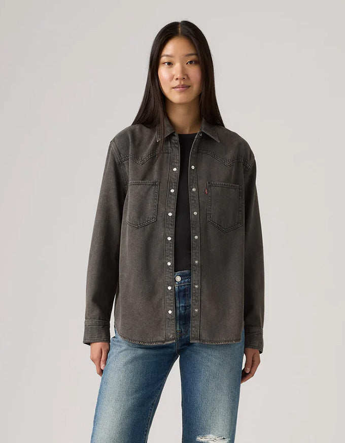 Person wearing a dark denim jacket and blue jeans on a light gray background