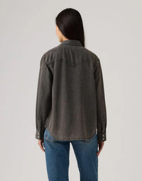 Person wearing a dark denim jacket and blue jeans on a light gray background