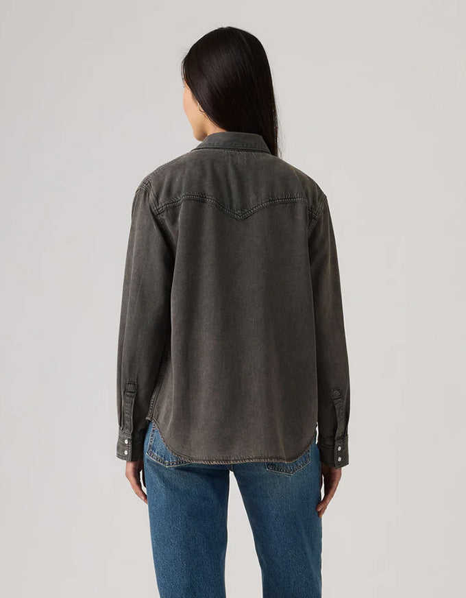 Person wearing a dark denim jacket and blue jeans on a light gray background