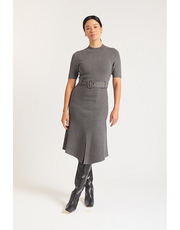 Woman wearing a gray dress with a belt and black boots on a white background