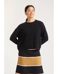 Woman wearing a black sweater and a black skirt with a gold band on a white background