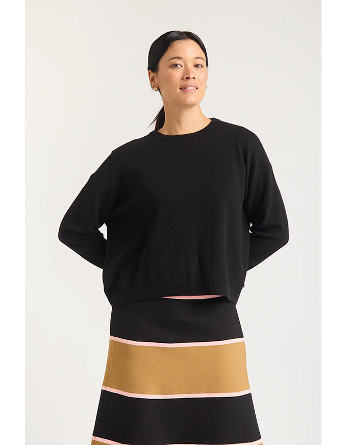 Woman wearing a black sweater and a black skirt with a gold band on a white background