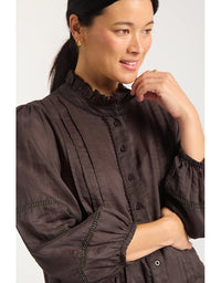 Woman wearing a dark brown blouse with long sleeves and buttons on a white background