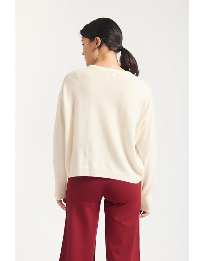 Woman wearing a cream sweater and red pants on a white background