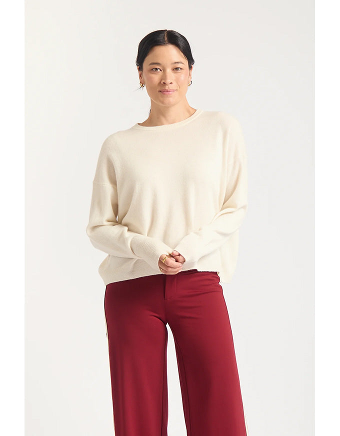 Woman wearing a cream sweater and red pants on a white background