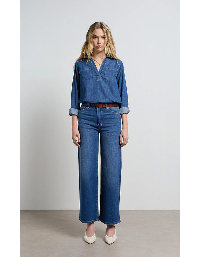 Woman wearing a blue denim outfit with wide-leg jeans on a plain background