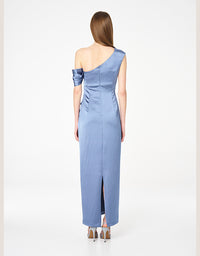 A woman viewed from the back wearing a one-shoulder midi dress in a dusty light blue satin-like fabric, paired with metallic high heels, against a plain white studio background.