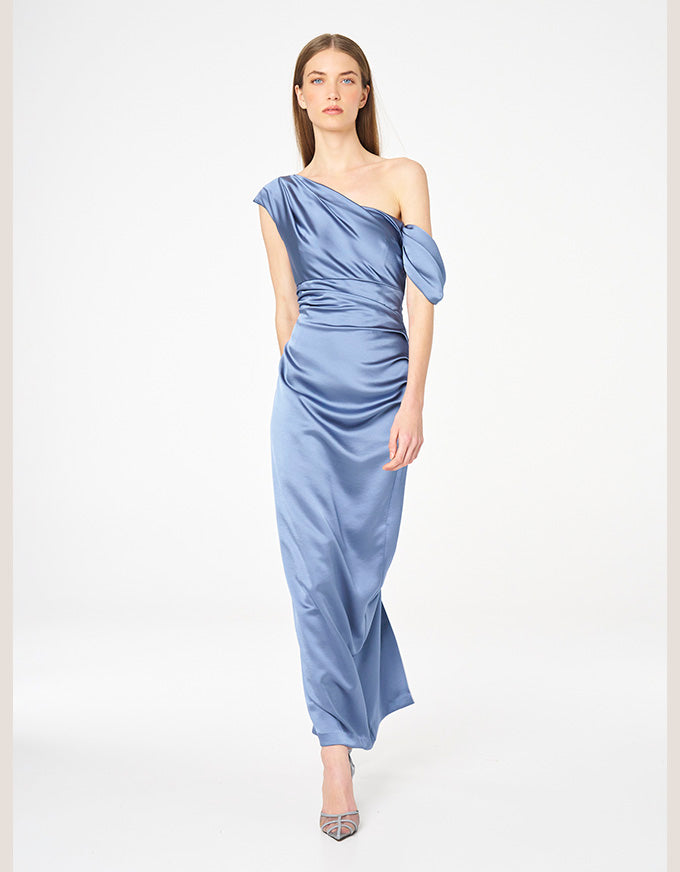 A woman modeling a light blue satin one-shoulder midi dress with a draped, gathered bodice and a flowing skirt, paired with pointed-toe heels, against a plain white studio background.