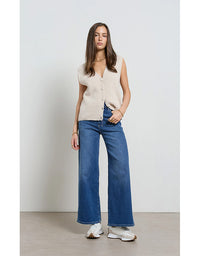 Woman wearing a sleeveless beige top and blue jeans against a white background