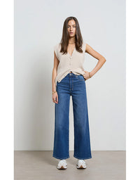 Woman wearing a beige sleeveless top and blue jeans against a white background