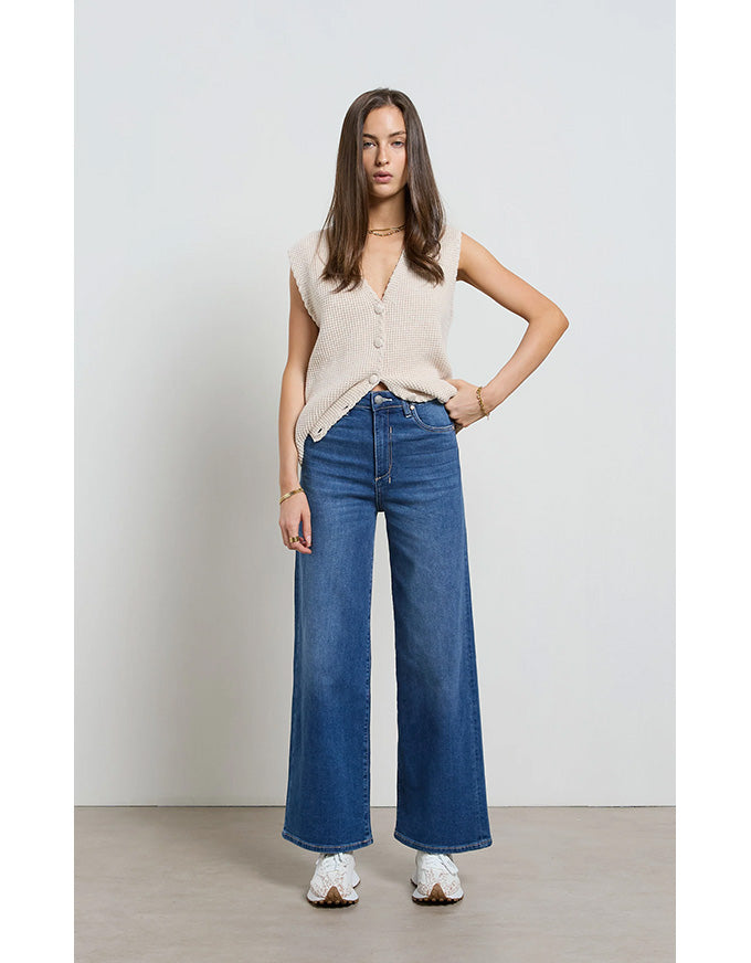 Woman wearing a beige sleeveless top and blue jeans against a white background