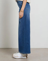 Person wearing blue jeans and white sneakers on a plain background