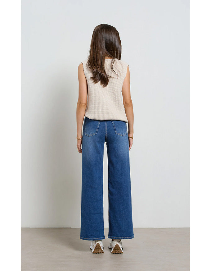 Person wearing blue jeans and a beige sleeveless top against a white background