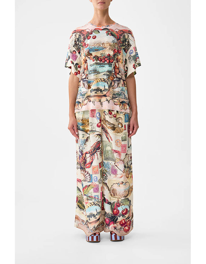 Person wearing a colorful patterned outfit on a white background. Notes From The Road Side Split Tee