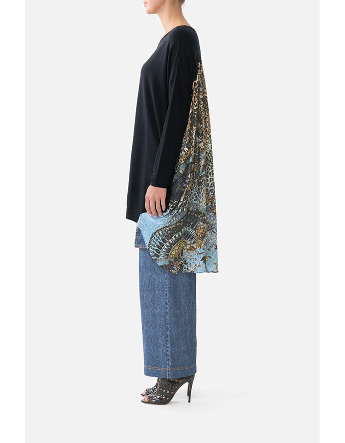 Person wearing a black top and blue jeans with a patterned scarf draped over one shoulder on a white background