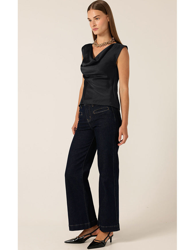 Woman wearing a black sleeveless top and dark jeans on a beige background