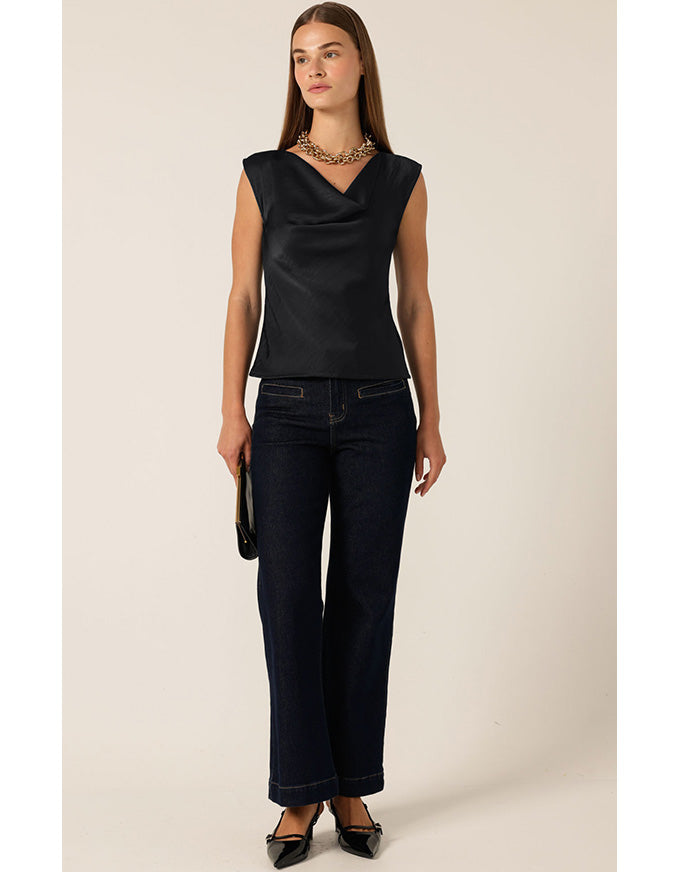 Woman wearing a black sleeveless top and dark jeans on a beige background