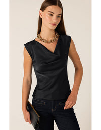 Woman wearing a black sleeveless top and dark jeans with a gold clutch against a beige background
