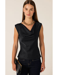 Woman wearing a black sleeveless top and dark jeans with a gold necklace on a beige background