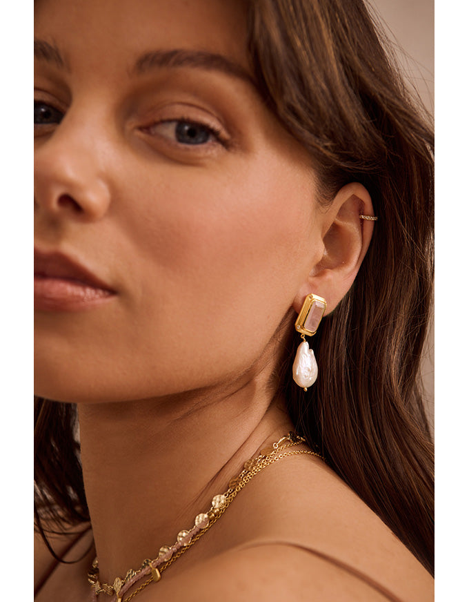 Close-up of a woman wearing gold earrings and a necklace with a neutral background