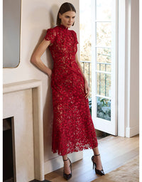 Woman in a red lace dress standing in a room with a fireplace and large window.