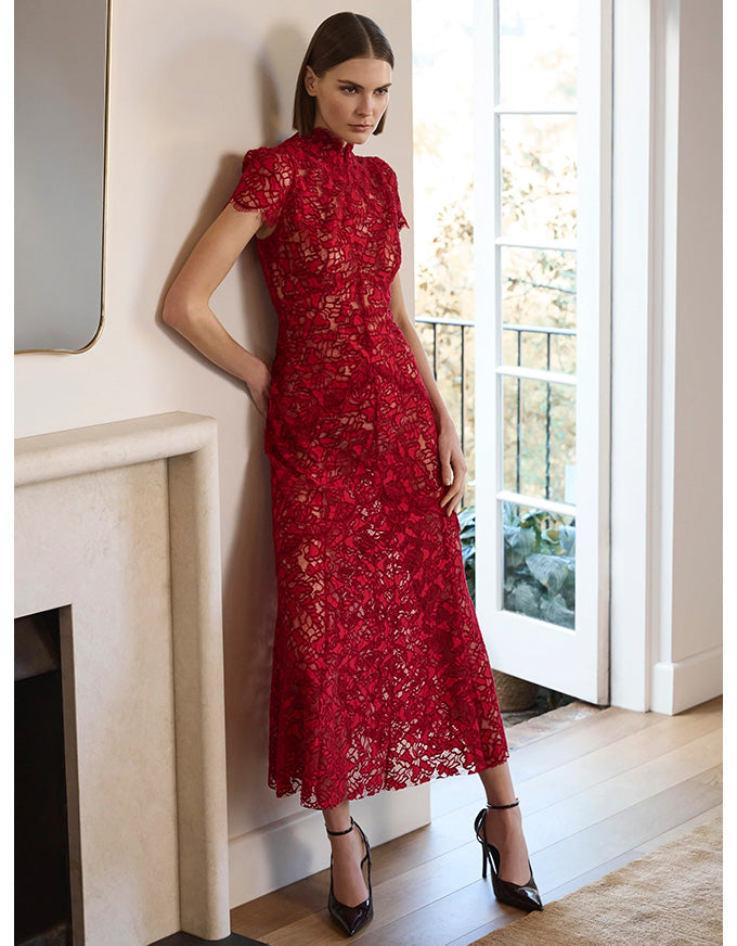 Woman in a red lace dress standing in a room with a fireplace and large window.
