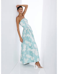 A woman models a strapless light blue maxi dress with a white floral pattern, standing in a minimalist white studio setting.