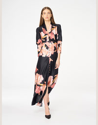 A woman modeling a black satin-like midi dress with a pink and peach floral print, standing against a plain white studio background.