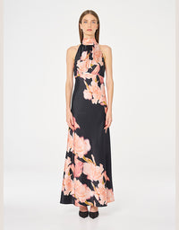 A model wearing a sleeveless halter-neck maxi dress with a black base and a large pink floral print, standing against a plain white studio background.