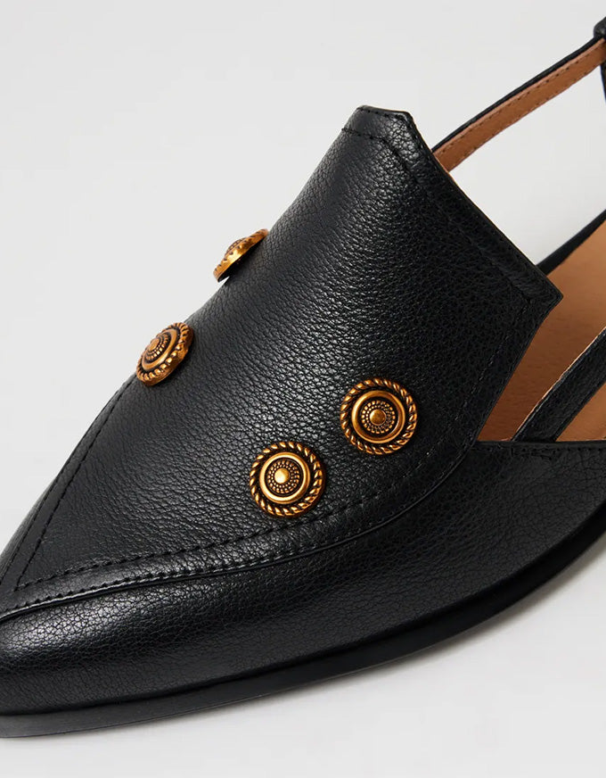 Black pointed-toe shoe with gold buttons on a light gray background
